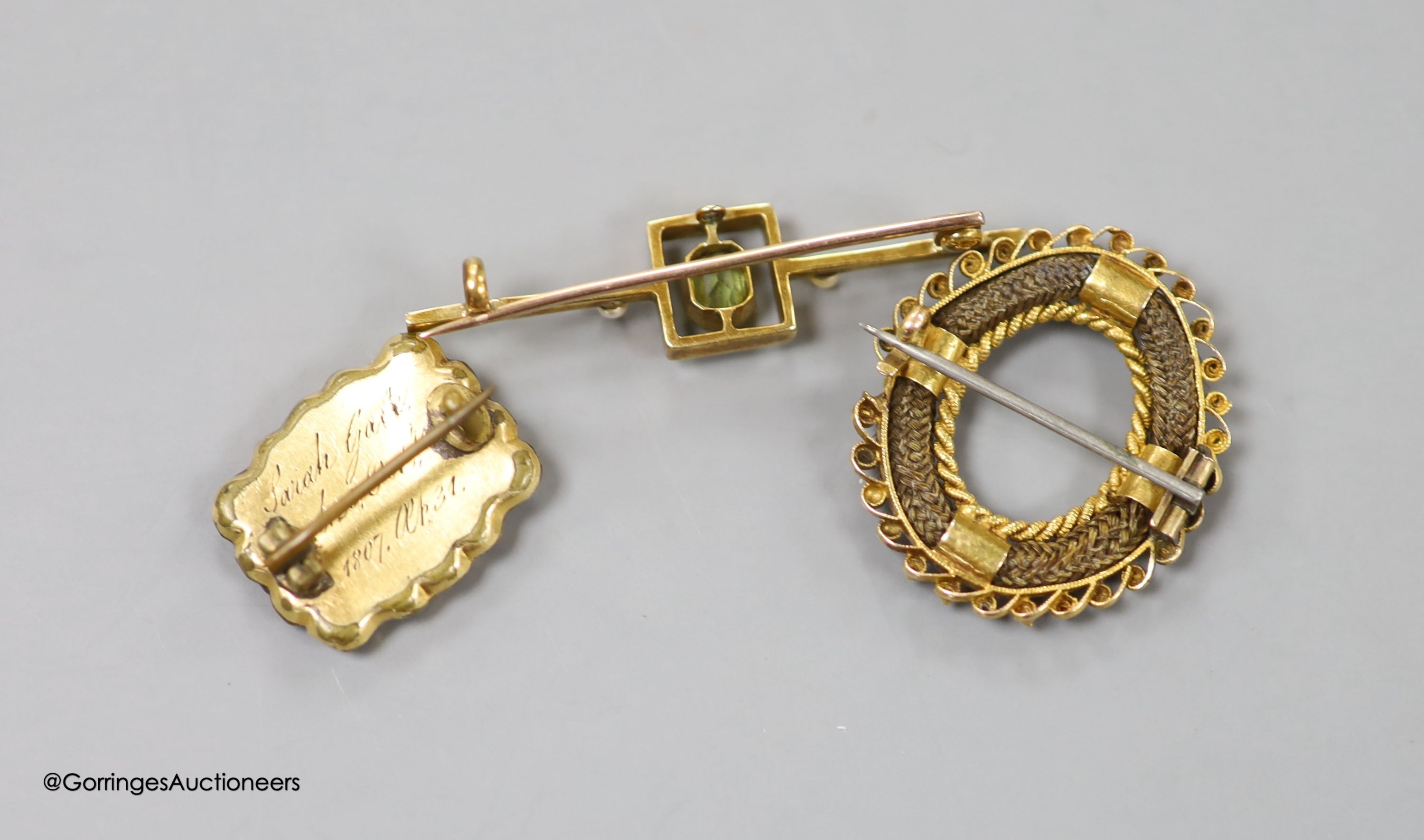 A George III gold plated mourning brooch, 20mm, a 19th century yellow metal and plaited hair openwork brooch, and an early 20th century yellow metal, peridot, seed pearl and white enamel set bar brooch, 42mm, gross 2.8 g